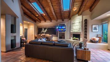 A spacious living area with a high ceiling and skylights, a comfortable sofa, a dining area, and a fireplace.