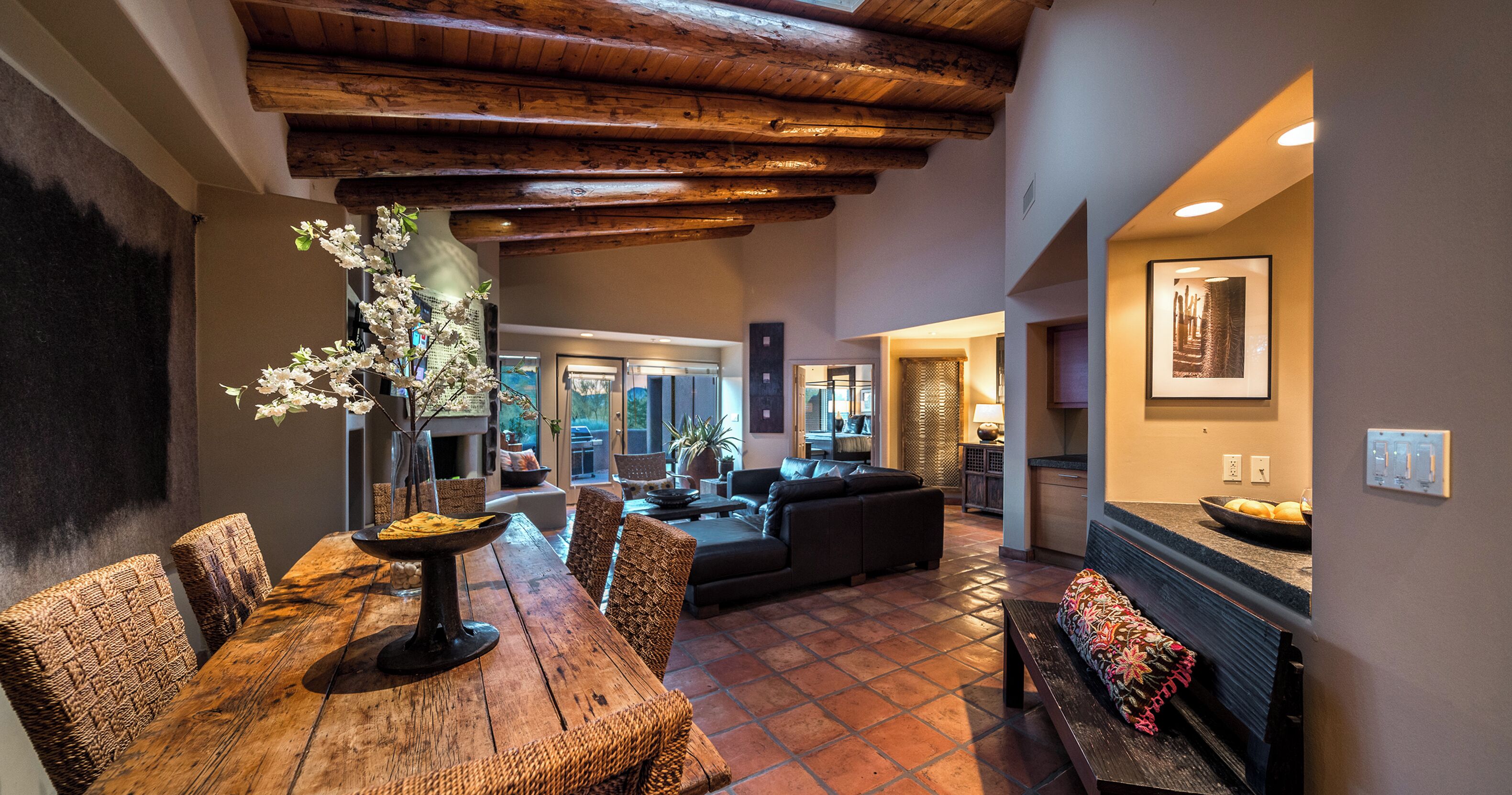 A spacious living area with a wooden dining table, wicker chairs, a sofa, and a fireplace.