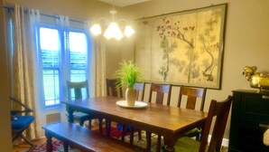 A dining area with a wooden table, chairs, a bench, a potted plant, a chandelier, and a wall painting. - Exquisite 2BR Luxurious Suite Great location in Greenville (Greenville)
