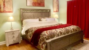 A bedroom with a wooden bed, two bedside tables, a red curtain, and wall art. - Exquisite 2BR Luxurious Suite Great location in Greenville (Greenville)