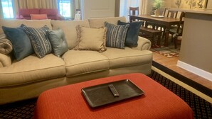 A living room with a beige sofa, red ottoman, and a dining area with a wooden table and chairs. - Exquisite 2BR Luxurious Suite Great location in Greenville (Greenville)