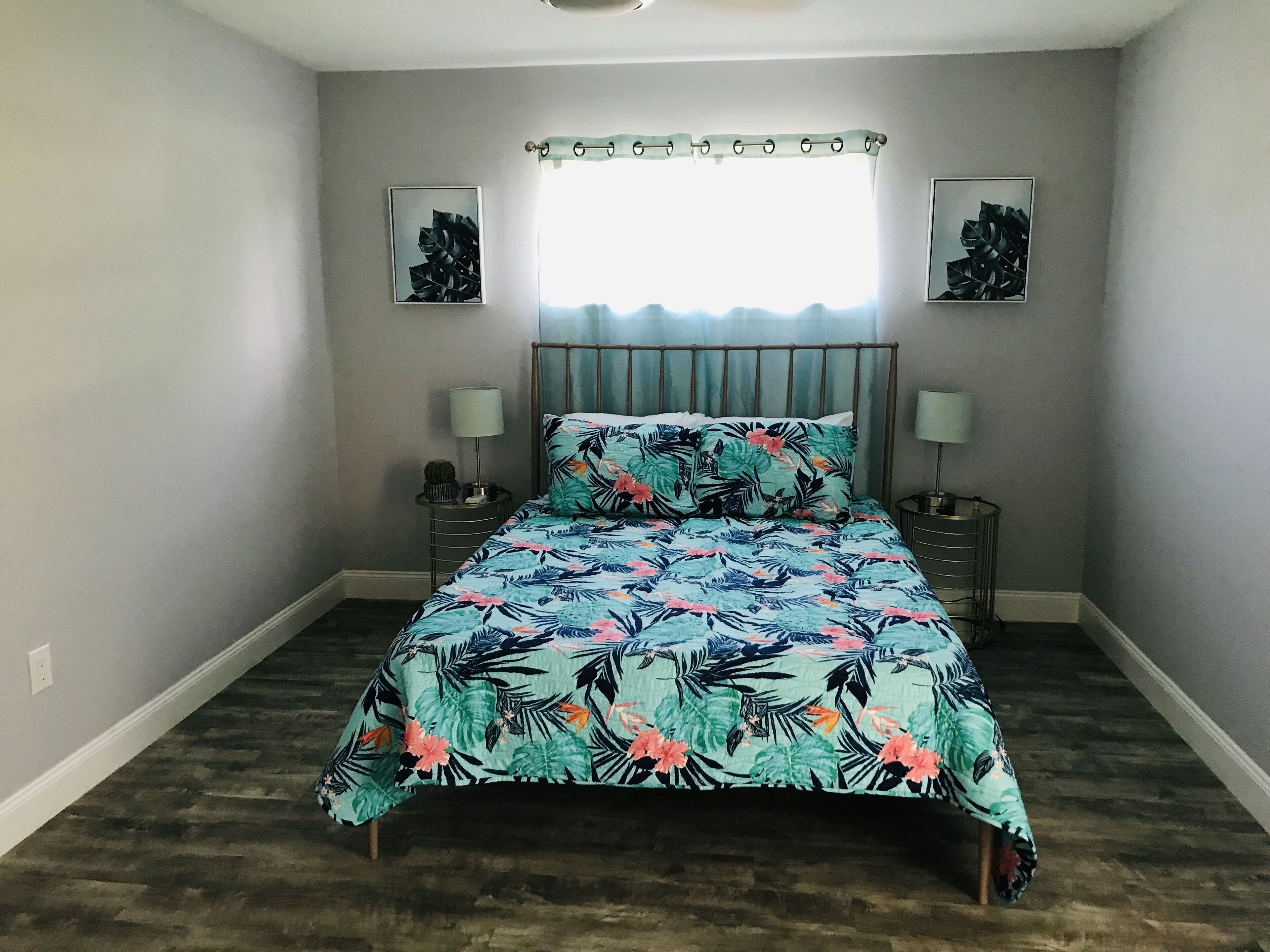 Une chambre à coucher comprenant un lit, deux tables de chevet, une fenêtre avec des rideaux et deux tableaux accrochés au mur.