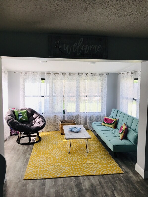 Un salon chaleureux avec un fauteuil noir, un canapé turquoise et un tapis jaune à motifs.