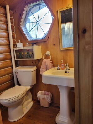 A compact bathroom with a toilet, sink, and window. - Cabin in the Country (Buffalo)