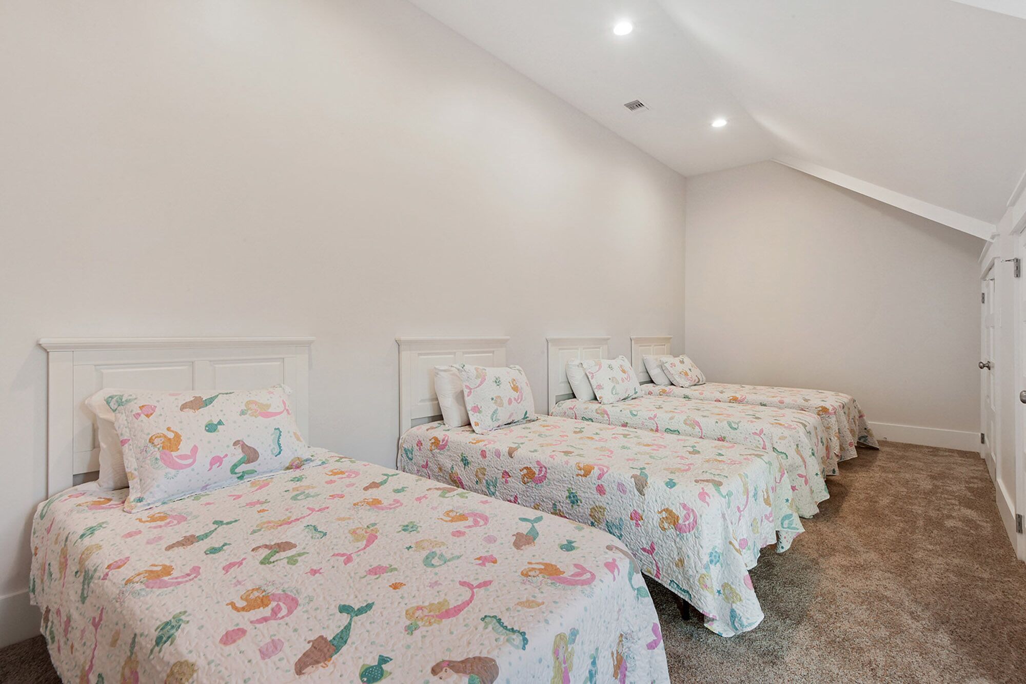 Een slaapkamer met vier bedden, elk met een kleurrijke bedspread met dierenprint en passend kussen. De kamer heeft witte muren en een schuine plafond met inbouwverlichting.