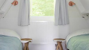 Ein Schlafzimmer mit zwei Betten, einem Fenster mit Vorhängen, einem Heizkörper und einer Wandleuchte.