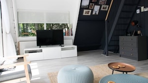 Ein modernes Wohnzimmer mit großem Fernseher, weißen Möbeln, einer dunklen Akzentwand und einer Treppe.