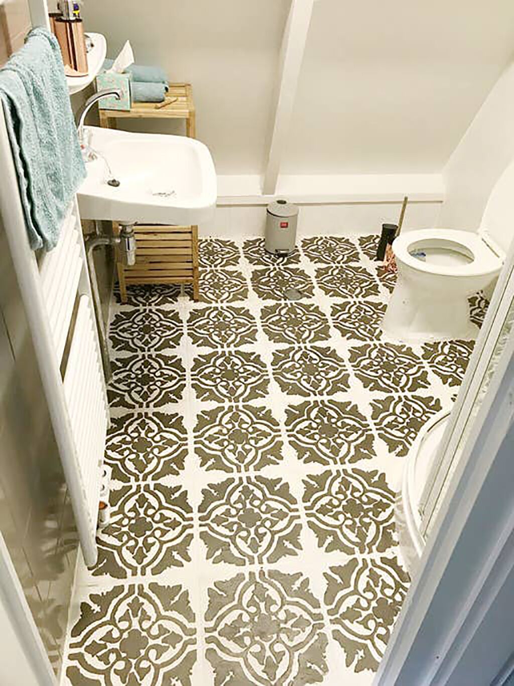 Une salle de bain avec des carreaux de sol à motifs, un lavabo blanc, des toilettes et une serviette accrochée au mur.