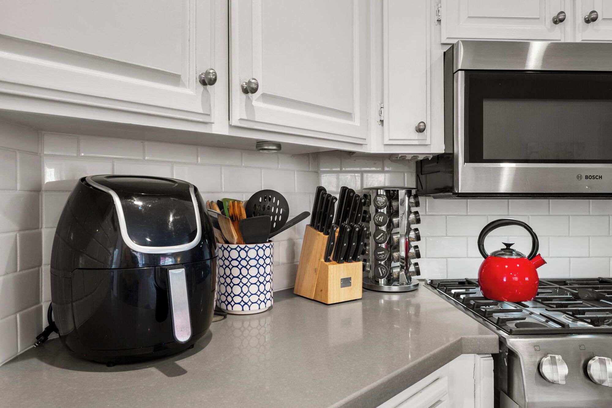A kitchen with white cabinets, a black kettle, a red teapot, and a knife block.