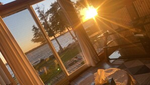 A room with a large glass window overlooking a body of water, a wooden deck, and a table with a chair.