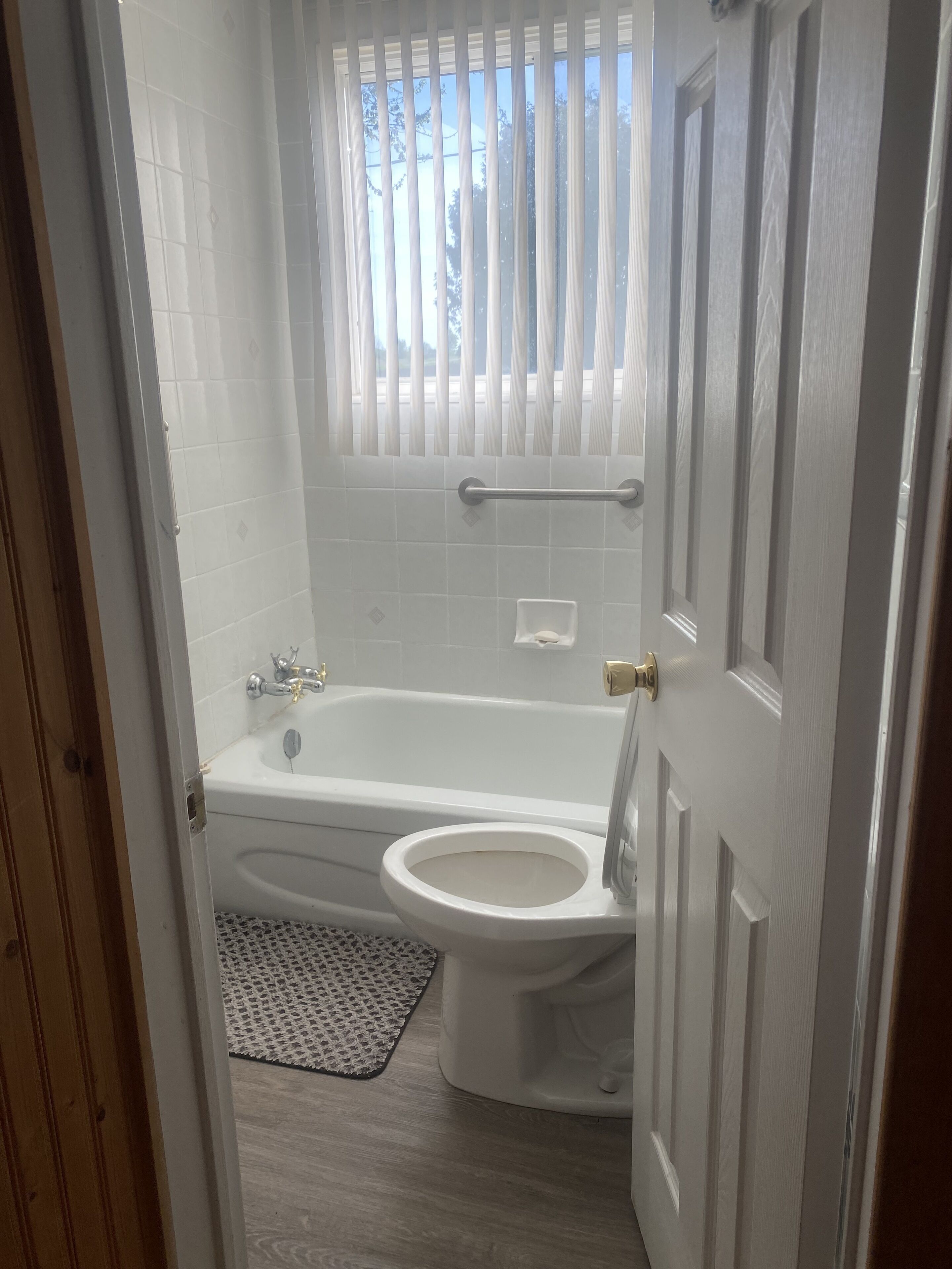 A bathroom with a bathtub, toilet, and a window with blinds.