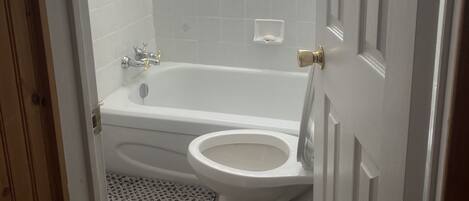 A bathroom with a bathtub, toilet, and a window with blinds.