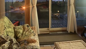 A room with a large sliding glass door leading to a deck, a sofa with a leopard print cover, and a small table with a water bottle and a bag.
