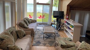 A cozy living room with a large window overlooking a lake, furnished with a sofa, chairs, and a TV.