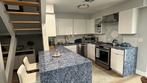 Una cocina moderna con una isla de mármol, electrodomésticos integrados y una escalera de madera.
