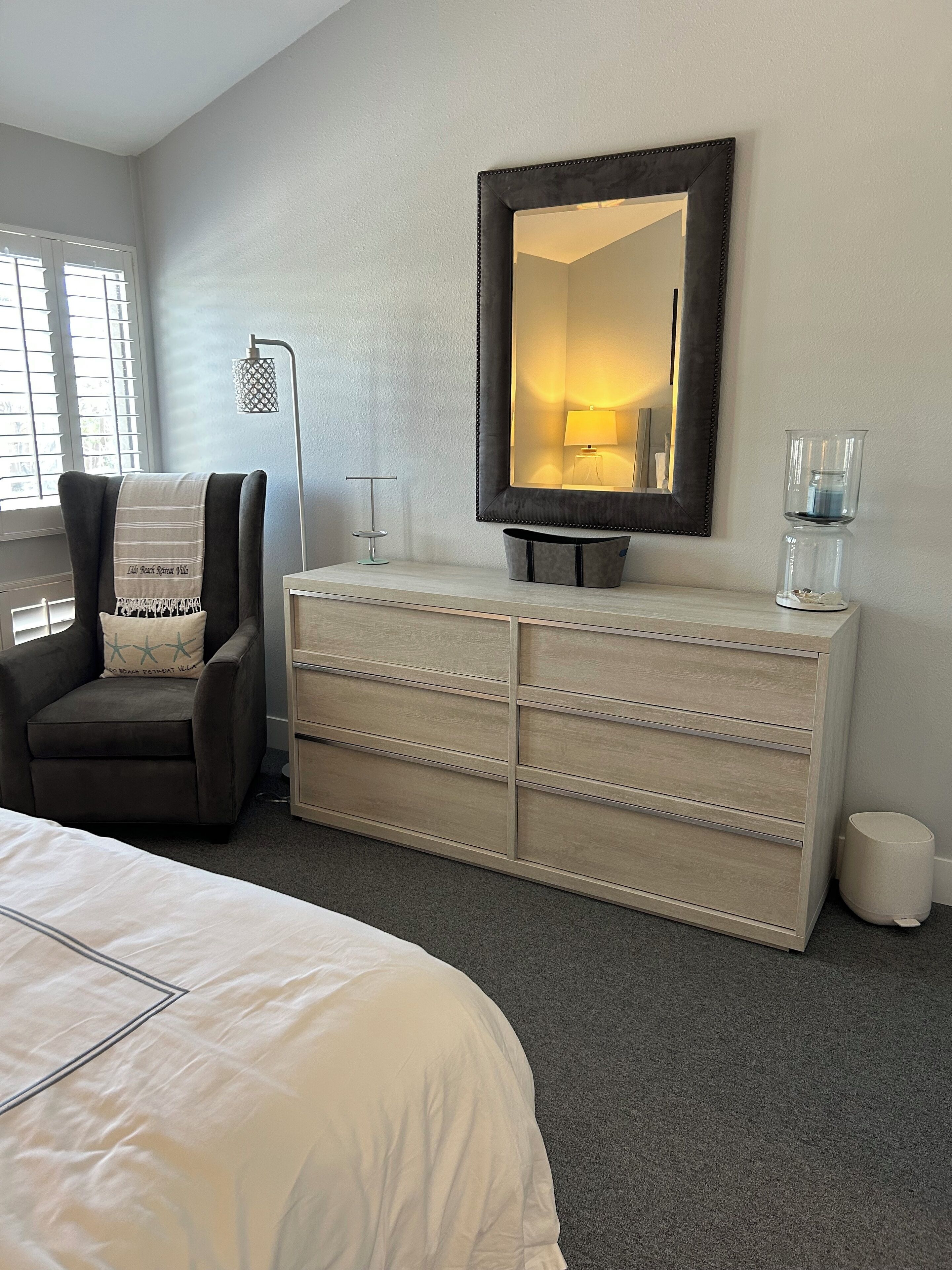 Una habitación de hotel con cama, cómoda, silla, espejo y lámpara.