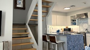 Una cocina moderna con microondas integrado, un lavabo y una estufa. Se ve una escalera de madera que sube a un nivel superior.