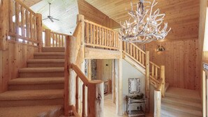 Un intérieur en bois avec un escalier, un lustre et un ventilateur de plafond.