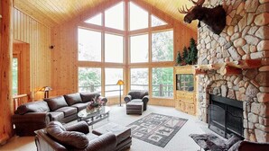 L’intérieur d’une cabane en rondins, avec une cheminée en pierre, des meubles en cuir et de grandes fenêtres.