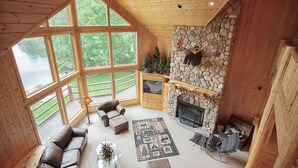 Un intérieur de chalet chaleureux avec une cheminée en pierre, un canapé en cuir et de grandes fenêtres donnant sur un lac.