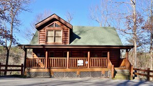 A log cabin with a green roof, wooden porch, and a small staircase leading to the entrance. - #1  (AMAZING GATED COMMUNITY) - YOUR OWN PRIVATE (SAUNA & HOTTUB) ON BACK DECK (Sevierville)