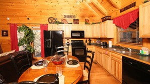 A wooden cabin kitchen with a dining table, chairs, a refrigerator, microwave, oven, and a sink. - #1  (AMAZING GATED COMMUNITY) - YOUR OWN PRIVATE (SAUNA & HOTTUB) ON BACK DECK (Sevierville)