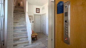 A wooden staircase leading to a door with an elevator control panel. - Waterfront Lux Private hot tub & elevator, marina (Port Aransas)