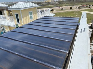 Un toit recouvert de panneaux métalliques, un immeuble jaune doté d’un balcon et une vue sur un aéroport situé au loin.
