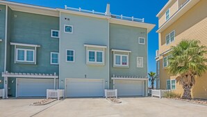 A multi-story residential building with a flat roof, multiple garage doors, and a white picket fence. - Waterfront Lux Private hot tub & elevator, marina (Port Aransas)