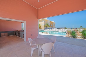 An outdoor patio with a dining table and chairs, a barbecue grill, and a view of a swimming pool and buildings in the background. - Waterfront Private Spa & elevator, Early Checkink (Port Aransas)