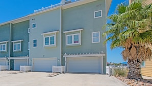 A multi-story residential building with a light blue exterior, white railings, and a palm tree in the foreground. - Waterfront Lux Private hot tub & elevator, marina (Port Aransas)