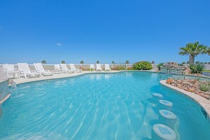 Une piscine à l’eau d’un bleu cristallin, entourée de chaises longues blanches et d’un palmier.