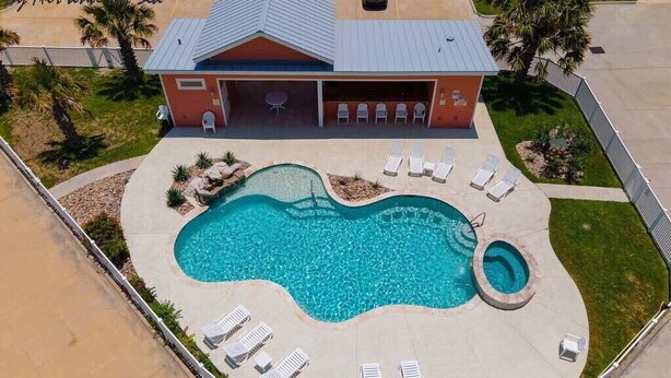 A swimming pool with lounge chairs and a building with a covered patio. - Waterfront Lux Private hot tub & elevator, marina (Port Aransas)