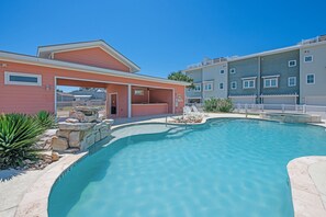 A residential building with a swimming pool, a covered patio, and a fenced area with lounge chairs.