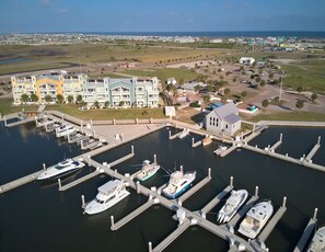 A marina with multiple boats docked, a small building, and a row of multi-story residential buildings with balconies.