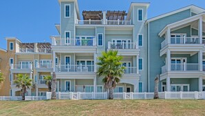 A multi-story hotel with balconies, a white picket fence, and palm trees in the foreground. - Waterfront Lux Private hot tub & elevator, marina (Port Aransas)