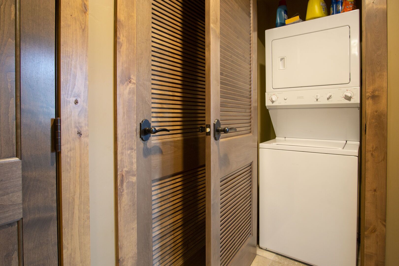 Un cuarto de lavado con lavadora y secadora blancas, puertas de madera y un respiradero con listones.