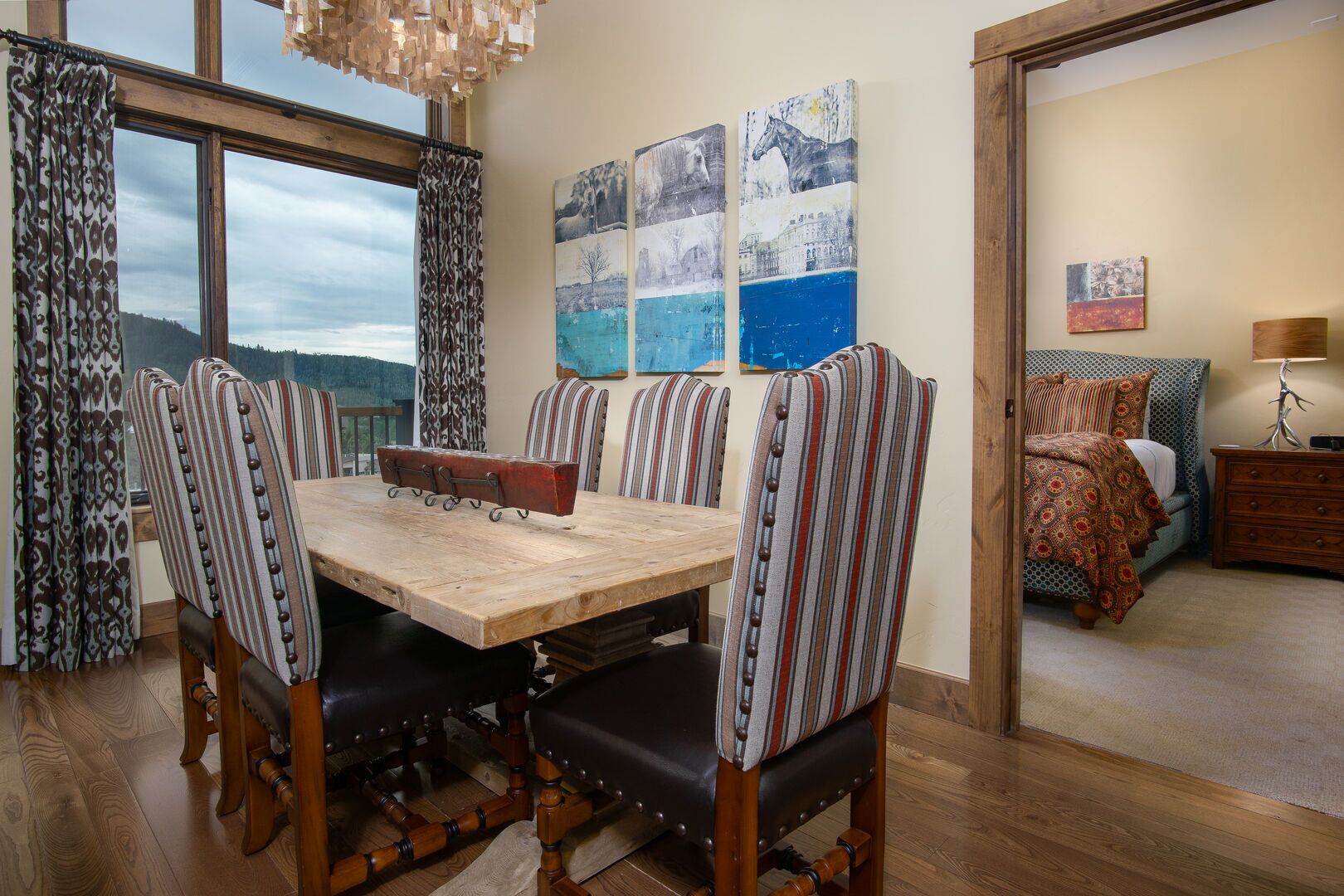 Comedor con mesa de madera, sillas tapizadas a rayas, un banco y vistas al exterior.