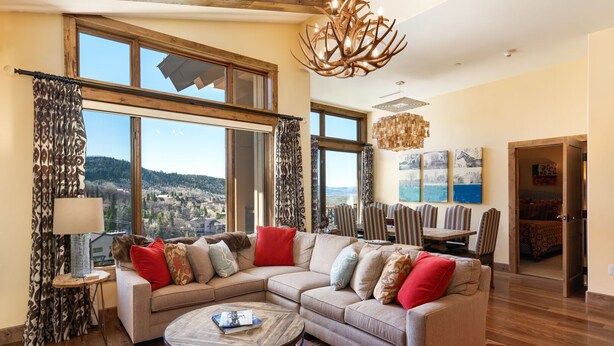 Un salon spacieux avec un grand canapé d’angle, une table basse ronde et une vue sur un paysage montagneux grâce à de grandes fenêtres.