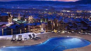 Une piscine avec des chaises longues et une vue sur la ville au crépuscule.