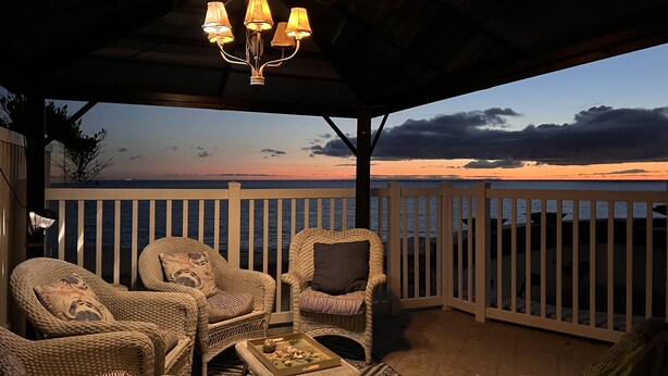 Zona relax all'aperto con mobili in vimini e vista sul tramonto sull'oceano.