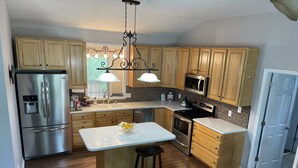 Une cuisine moderne avec des meubles en bois, des appareils en acier inoxydable, un îlot central et des luminaires suspendus.