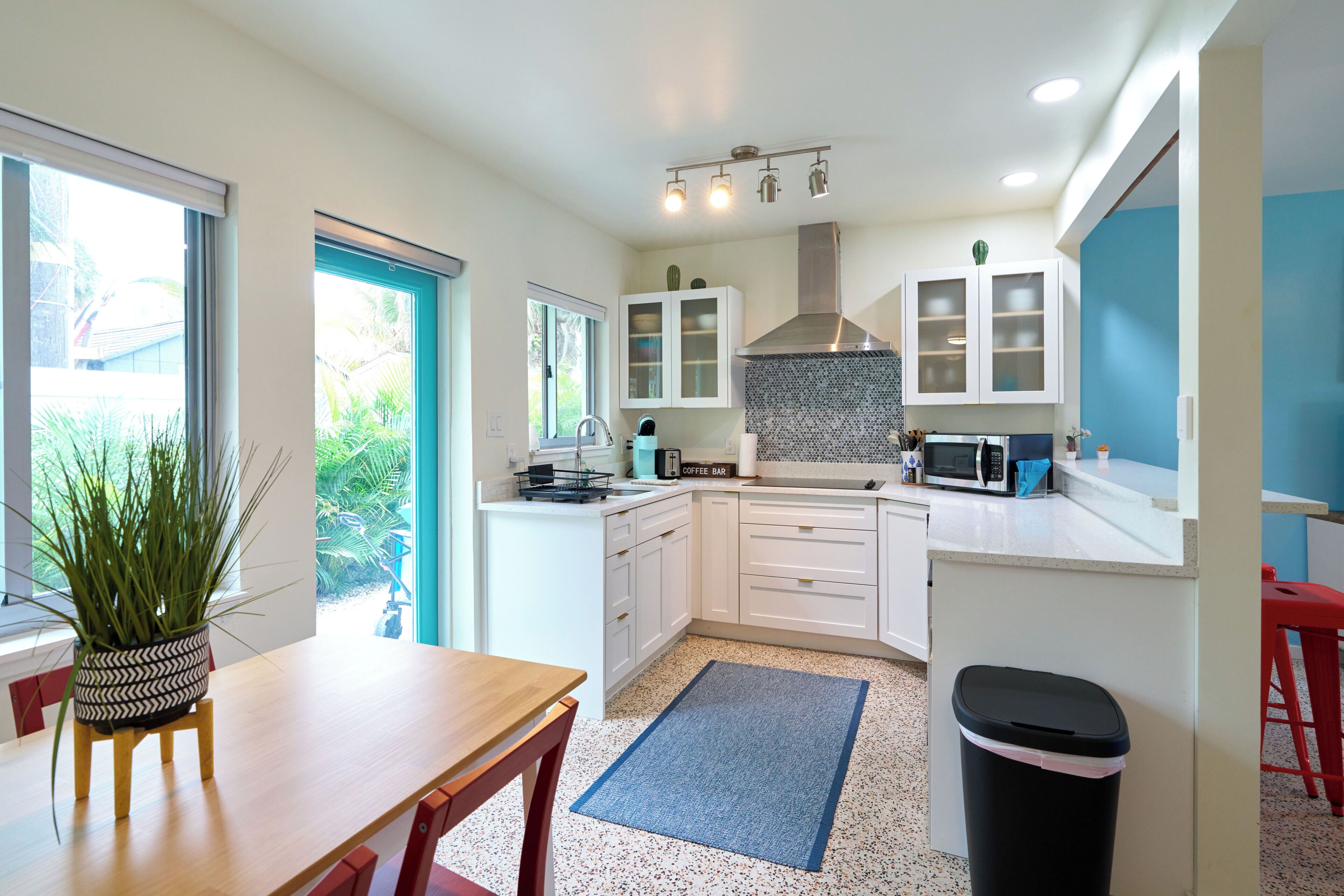 A modern kitchen with white cabinets, a stainless steel range hood, a microwave, and a coffee bar.
