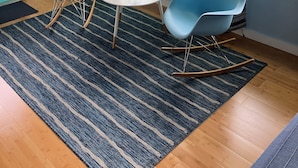 Une pièce avec deux chaises bleues, une petite table blanche, un tapis bleu et une fenêtre avec des rideaux.