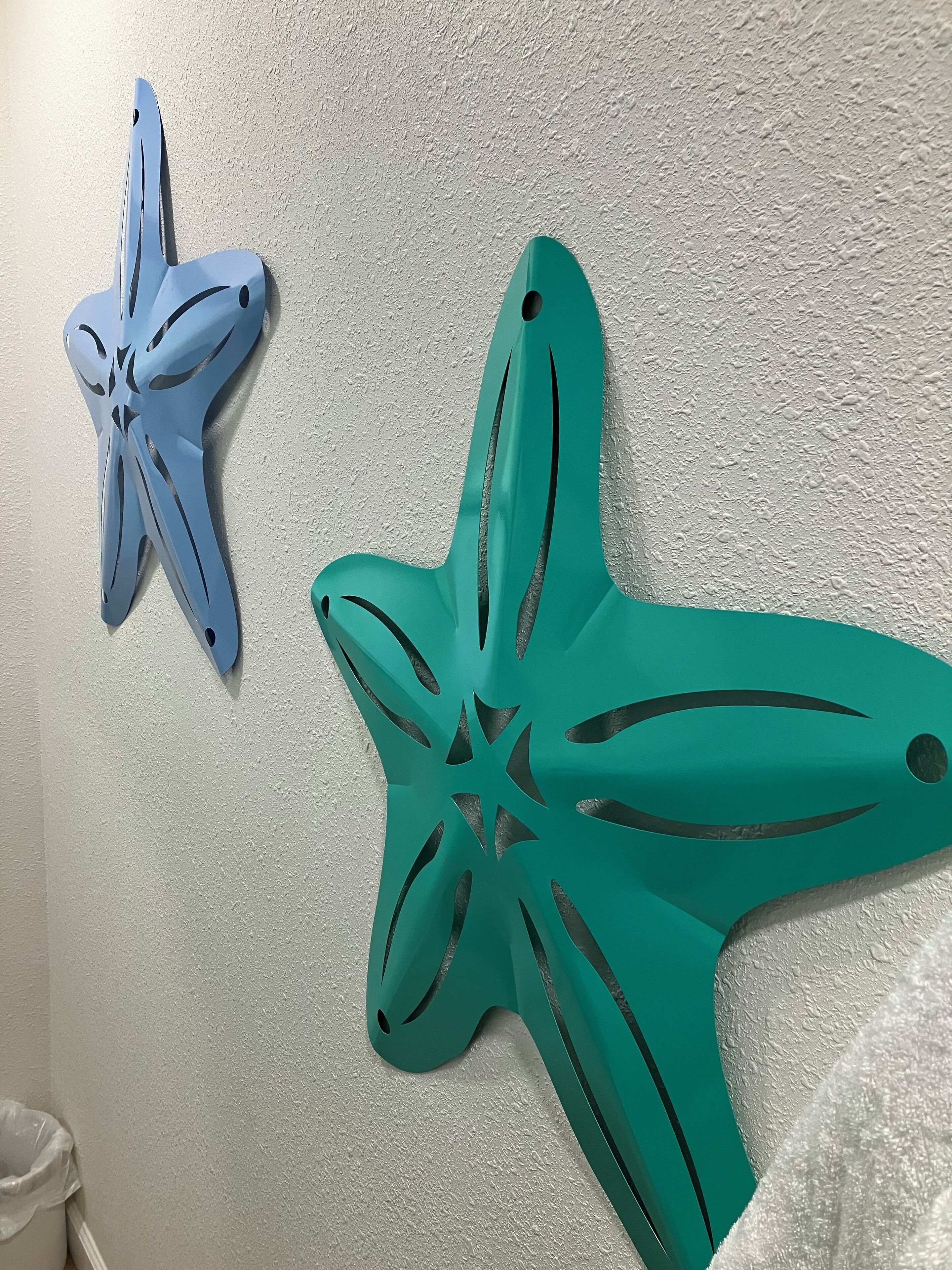 Two star-shaped wall decorations, one blue and one green, mounted on a textured wall.
