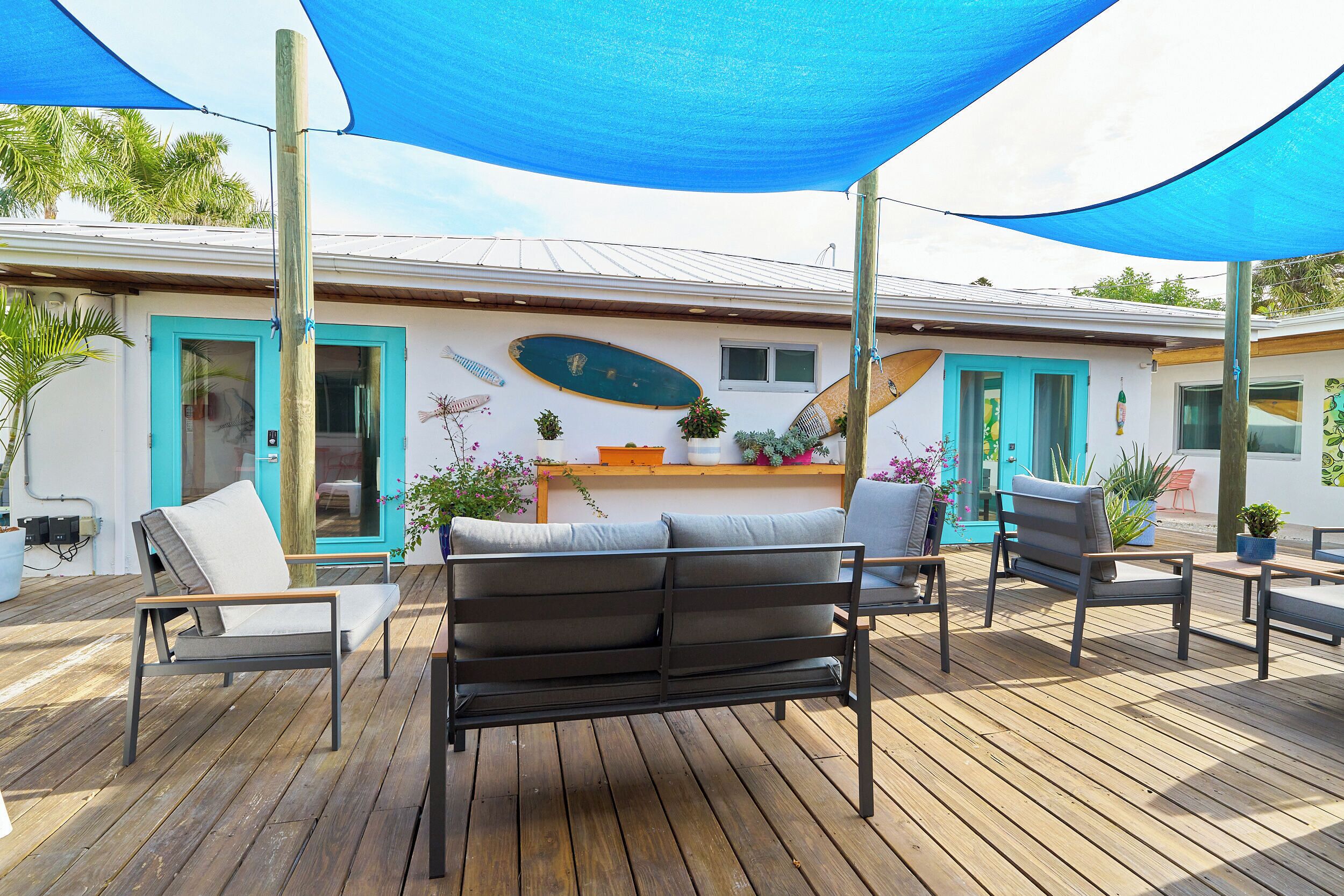 Une terrasse en bois avec des sièges extérieurs, un bâtiment blanc avec des portes turquoise et un auvent bleu.