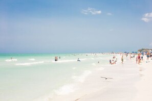 Uma praia com águas turquesa cristalinas e areia branca, cheia de gente.