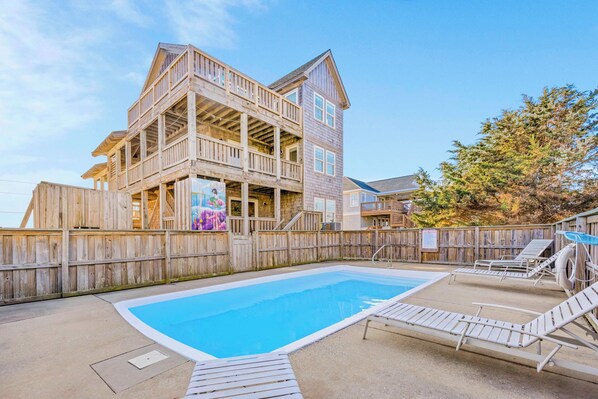 A wooden multi-story building with a swimming pool and lounge chairs.
