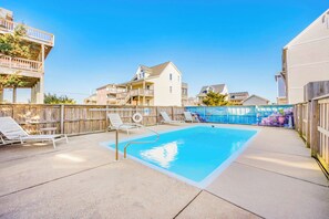 A backyard with a swimming pool, lounge chairs, and a wooden deck.