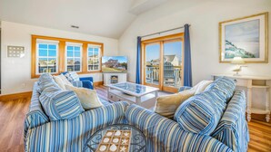 A spacious living room with striped sofas, a glass coffee table, and large windows offering a view of the neighborhood.